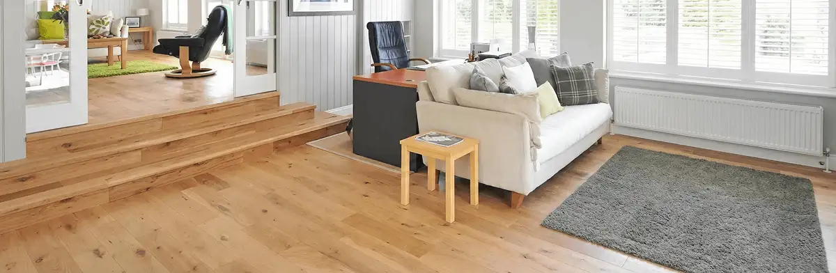 A modern living room with professionally installed laminate flooring, a beige sofa, a small side table, a gray rug, and large windows with white shutters in Chandler, AZ